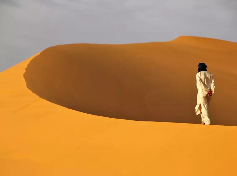 Person in traditioneller Kleidung wandert über eine Sanddüne in der Sahara.