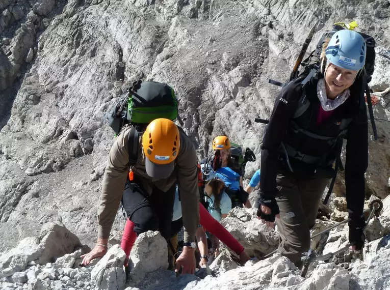 Mehrere Bergsteiger erklimmen steinigen Klettersteig mit Helmen und Rucksäcken.