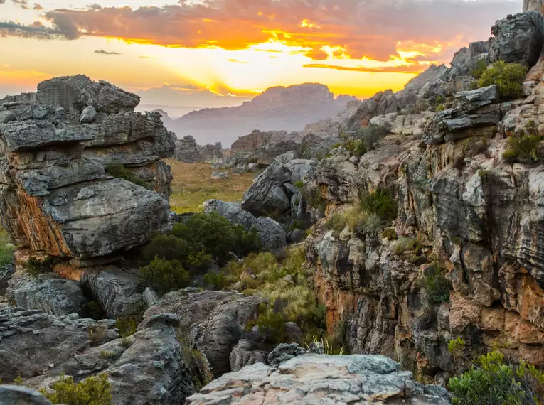 Südafrikanische Berglandschaft bei Sonnenuntergang mit Felsen und Vegetation.