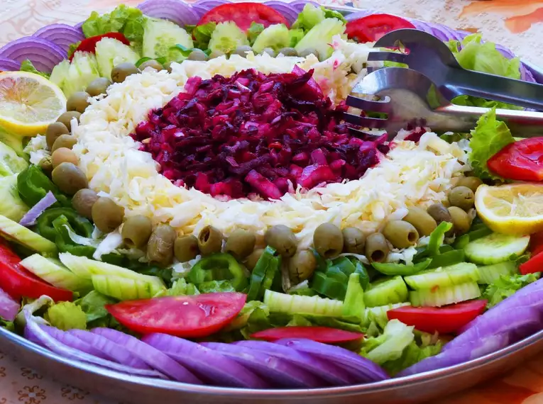 Bunte Gemüsesalatplatte mit Oliven, Tomaten und Zwiebeln auf einem runden Teller arrangiert.