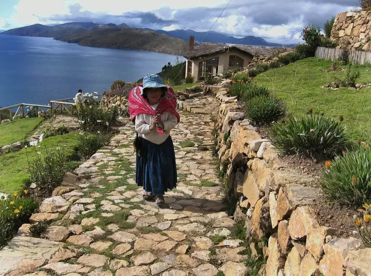 Frau in traditioneller Kleidung auf steinigem Pfad bei Isla del Sol, mit Blick auf den See.