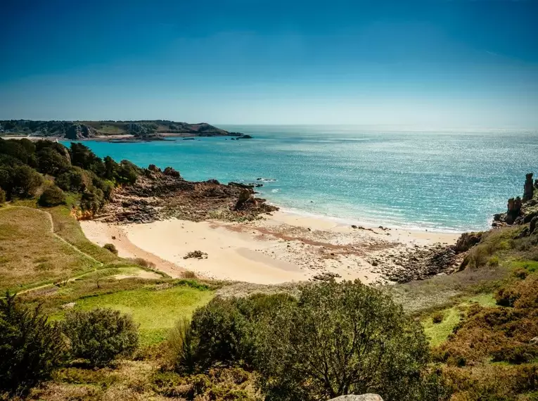 Blick auf die sandigen Buchten und grüne Küsten von Jersey unter blauem Himmel.