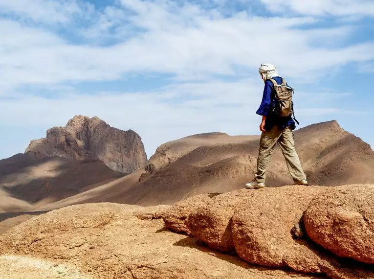 Ein Wanderer genießt den Ausblick auf die beeindruckende Wüstenlandschaft Algeriens mit felsigen Bergen im Hintergrund.