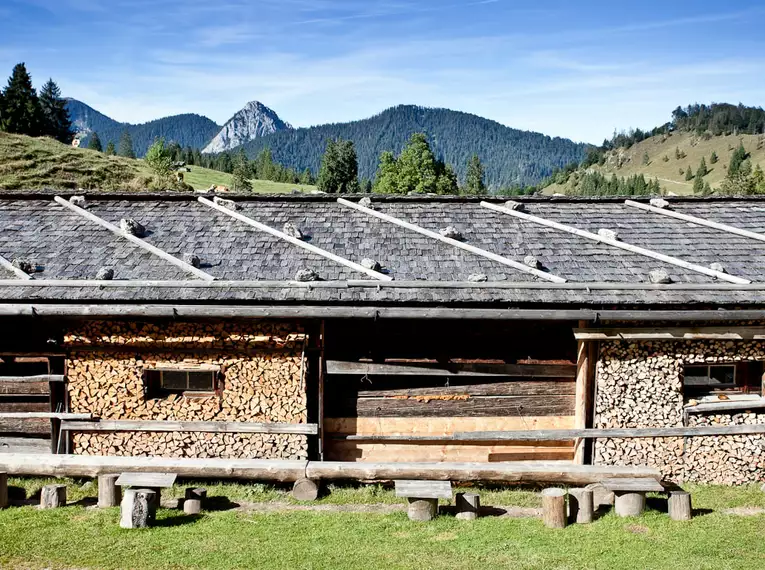 Urige Alm mit Holzstapeln und Bergkulisse in den Bayerischen Alpen.