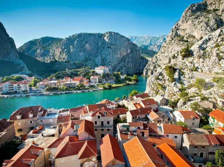 Malerisches Dorf mit roten Dächern am Meer und Bergen im Hintergrund.