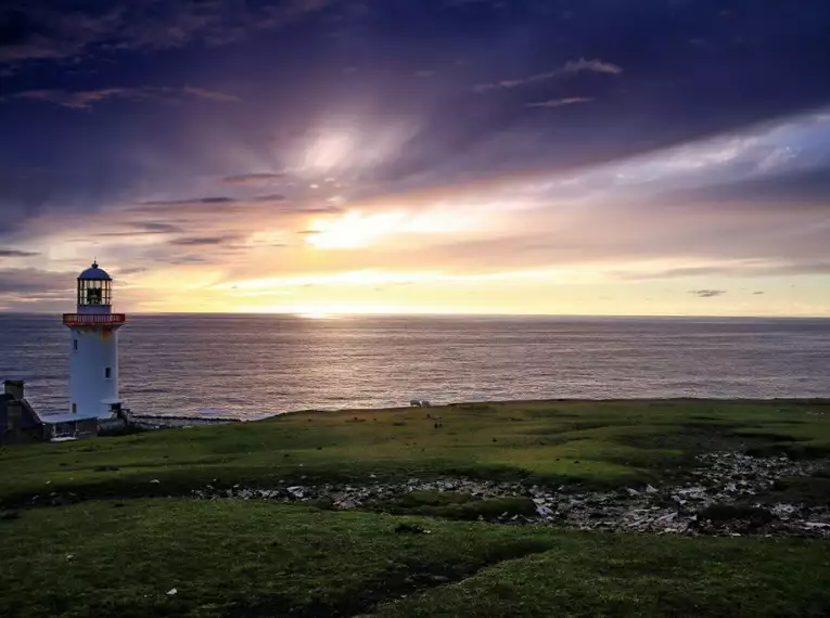 Landschaftsbild von einem Leuchtturm am Meer mit Sonnenuntergang in Irland.