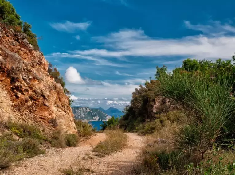 Steiniger Wanderweg auf Korfu mit Blick auf das blaue Meer unter blauem Himmel.