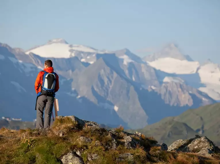 Ein Wanderer steht in den Alpen und blickt auf eine beeindruckende Bergkette.