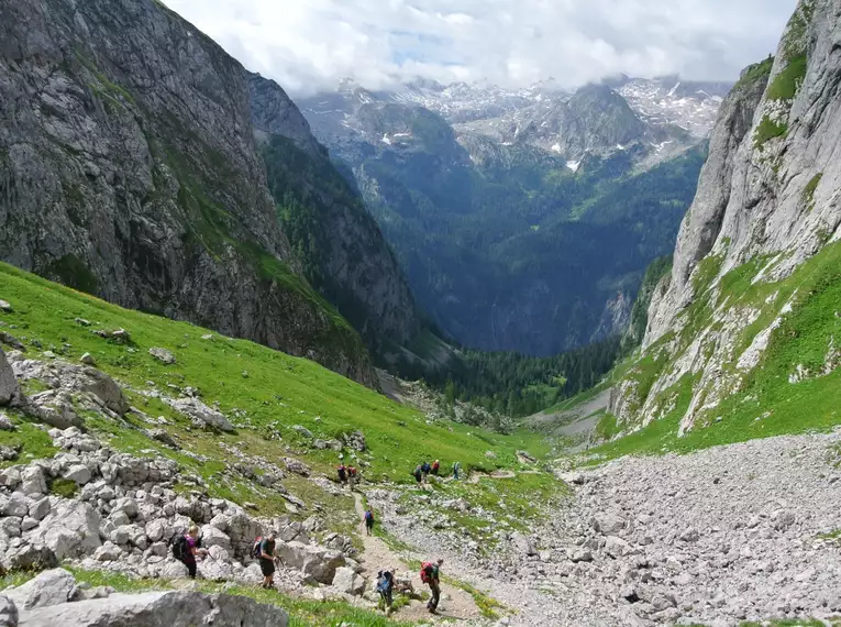 Wanderer im steinigen Gebirge mit grünen Wiesen und Bergblick.