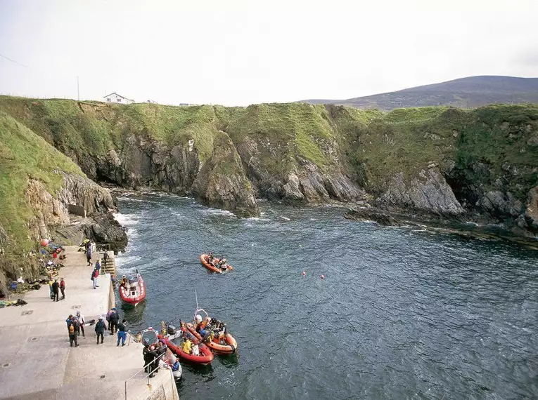 Boote und Menschen an der felsigen Küste von Arranmore Island, Irland.