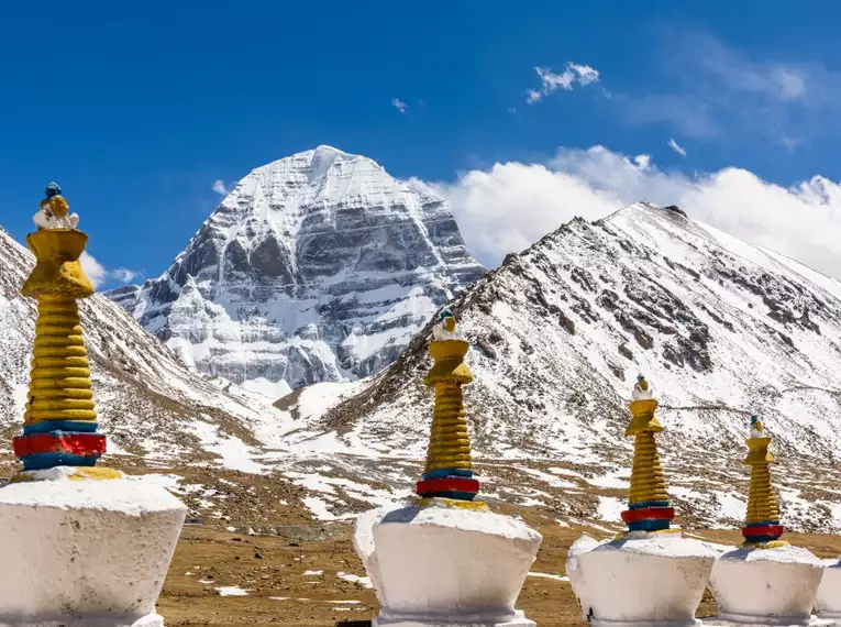 Der schneebedeckte Mount Kailash in Tibet mit Chörten im Vordergrund, blauer Himmel.