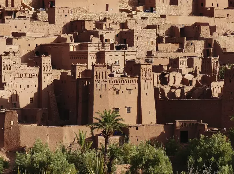 Ait Benhaddou mit traditionellen Lehmbauten und Palmen im Vordergrund.