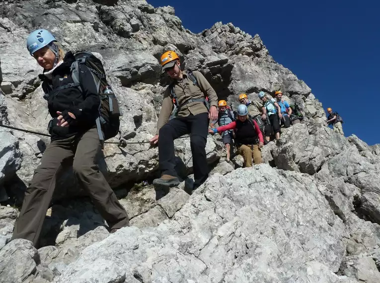 Gruppe von Bergsteigern auf felsigem Steig bei sonnigem Himmel unterwegs.