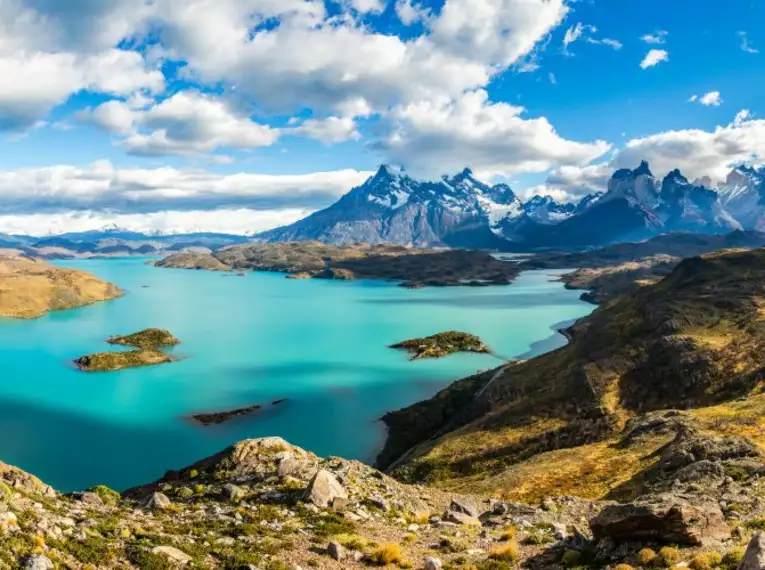 Panoramablick über den Torres del Paine Nationalpark mit Bergen und Seen unter einem wolkigen Himmel.