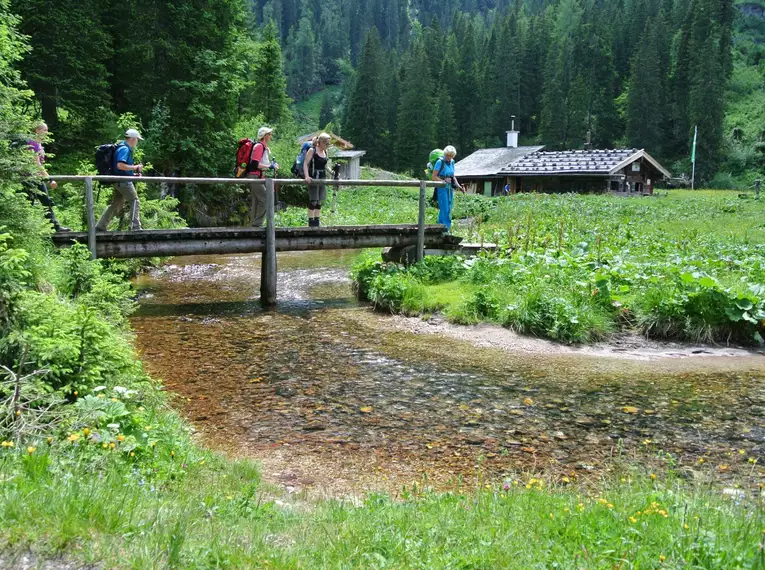 Gruppe von Wanderern überquert eine kleine Brücke in den Alpen.