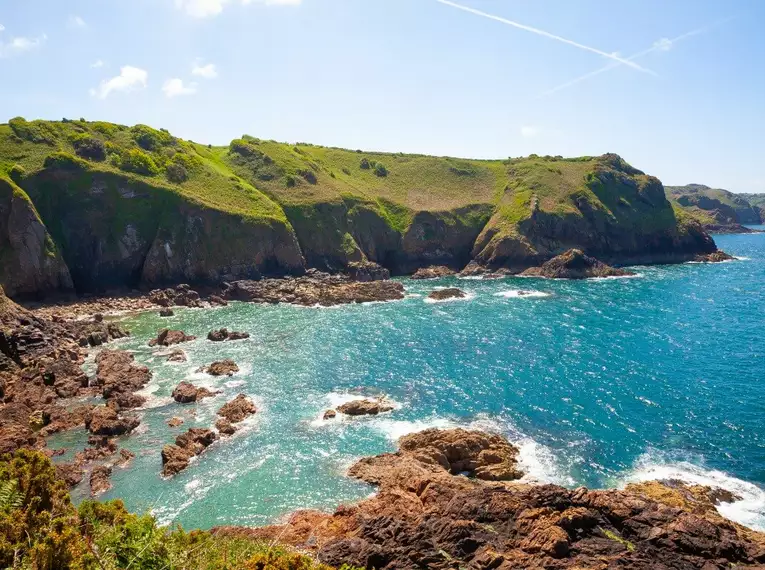 Klippenlandschaft auf Jersey, umgeben von blauem Meer und grünem Gras.