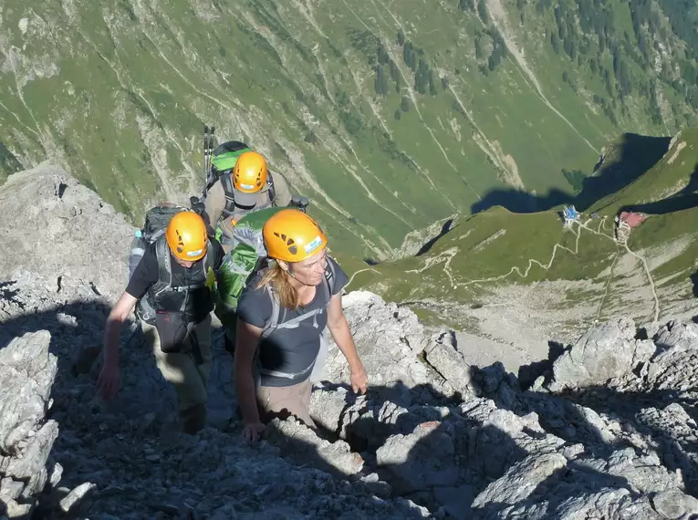 Drei Bergsteiger mit Helmen auf einem steilen Steig im Gebirge.