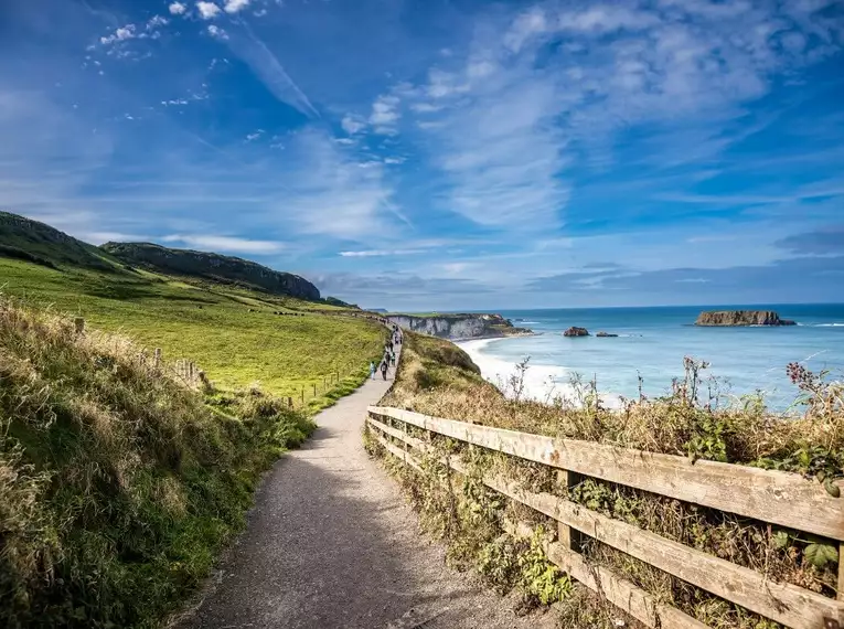 Küstenpfad in Irland mit blauem Himmel und Meer.