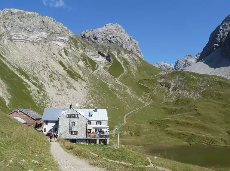 Eine Berghütte in alpiner Landschaft mit Bergpfaden und grünen Hängen.