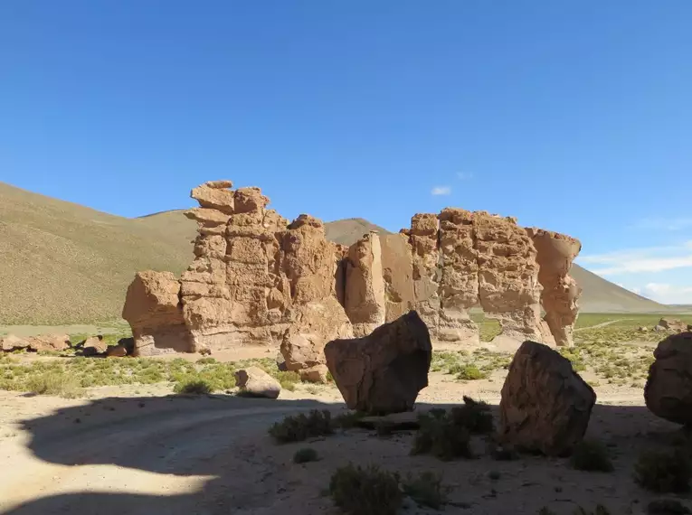 Rote Felsformationen unter blauem Himmel in der Atacama-Wüste, umgeben von trockener Vegetation.