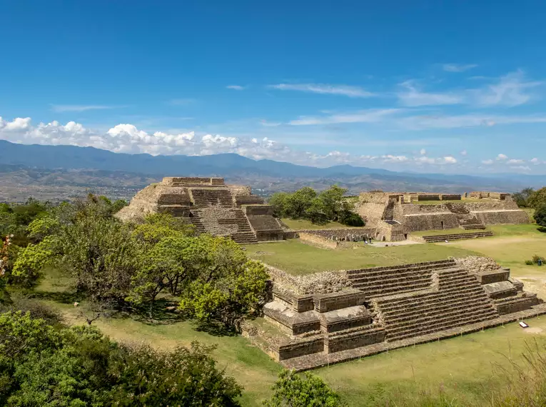 Maya-Ruinen von Monte Albán; steinige Terrassen und Pyramiden in üppiger Landschaft unter blauem Himmel.