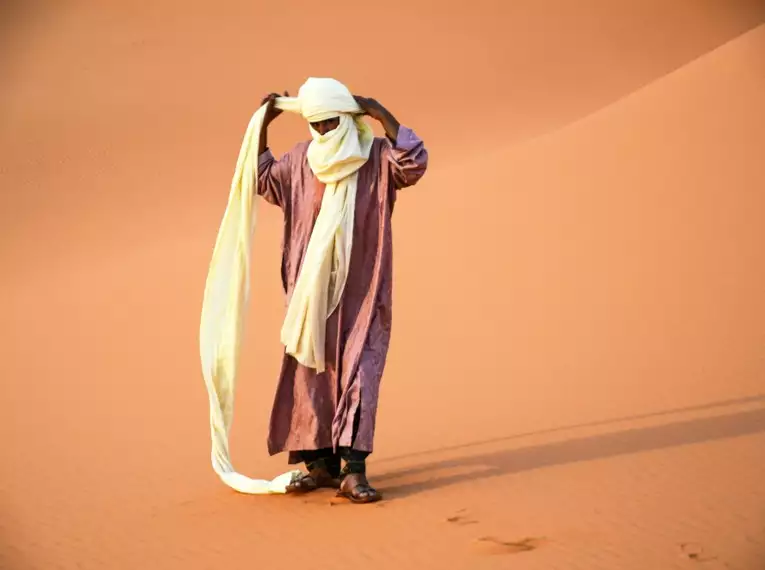 Ein Tuareg wickelt seinen Turban in der Wüstenlandschaft.