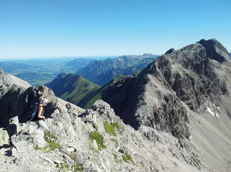 Wanderer auf felsigem Grat mit Alpenpanorama, blauer Himmel.