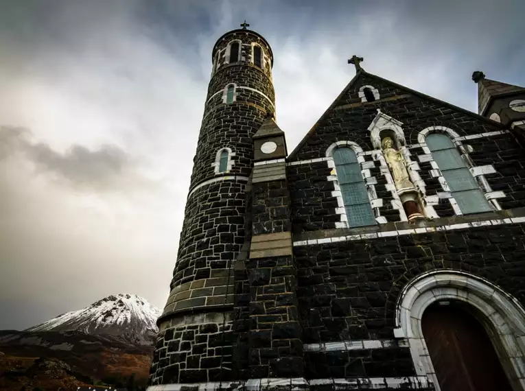 Eindrucksvolle Kirche vor dramatischer Berglandschaft in Irland