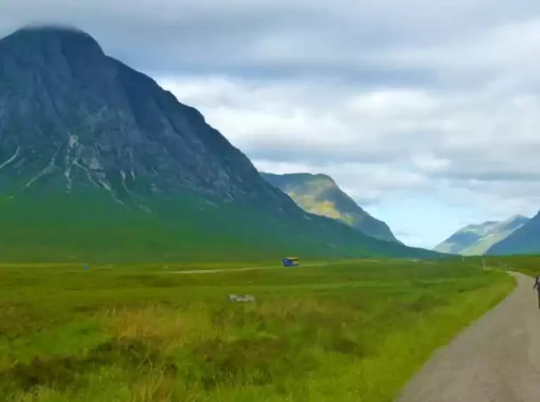 Ein Wanderer auf einem Pfad inmitten der schottischen Highlands mit grünen Bergen.