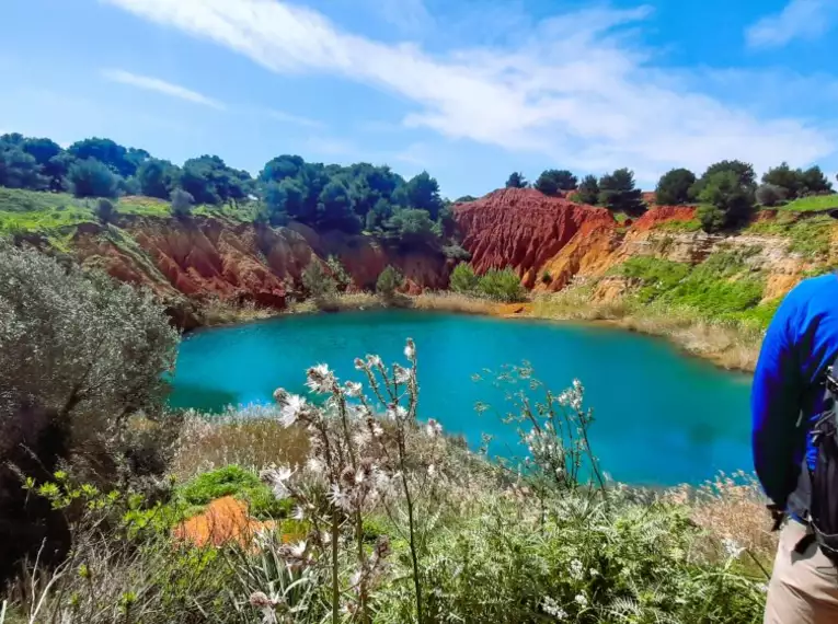 Wanderer betrachtet türkisblauen See in farbenfroher Landschaft in Apulien, Italien.